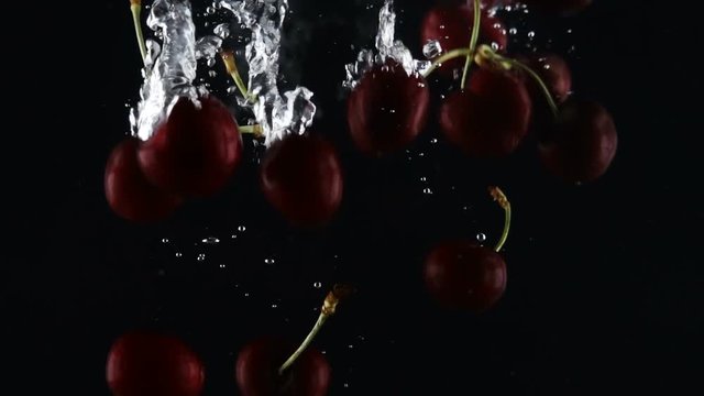 ripe dark red sweet cherry falls in water on a black background