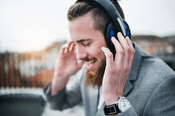 A young businessman with headphones on a terrace, listening to music.