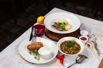 Top view of a three course set menu: beef stroganoff with mashed potatoes, turkey cutlet with rice and hot sorrel soup