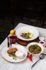 Top view of a three course set menu: beef stroganoff with mashed potatoes, roasted crunchy cutlet with rice and hot sorrel soup, served on a white wooden table
