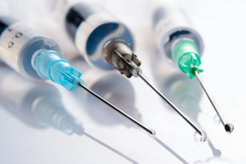 Three used syringes with medicinal solution, on light green background with reflection and water...