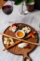 Assorted cheese for wine: bread sticks, bree, gouda, honey, parmesan, camembert and strawberries, served on a wooden board, on a black and white background