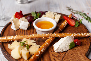 Close up of a perfect appetizer to wine: breadsticks, bree, gouda, honey, parmesan, camembert and strawberries, served on a wooden board