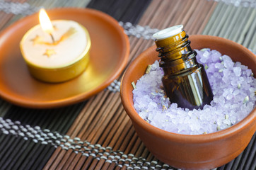 Obraz na płótnie Canvas Small bottle of essential oil in the bowl with aroma bath salt and burning candle. Aromatherapy, spa and herbal medicine concept. Close up, copy space.