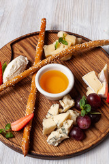Close up of gourmet appetizer – assorted cheese, grapes, strawberries, bread sticks and flower honey, served on a rustic wooden board