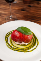 Bull's Heart tomato, stuffed with tuna and cheese, flavoured with fresh pesto sauce and basil on a white plate