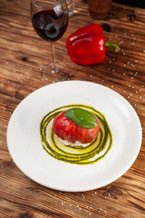 Bull's Heart tomato, stuffed with tuna and cheese, flavoured with fresh pesto sauce and basil on a white plate