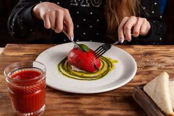 Woman is eating Bull's Heart tomato, stuffed with tuna and cheese, flavoured with fresh pesto sauce and basil on a white plate