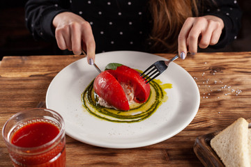 Woman is eating Bull's Heart tomato, stuffed with tuna and cheese, flavoured with fresh pesto sauce and basil on a white plate