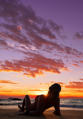 Naklejka na ściany i meble Woman sitting on the beach at sunset