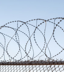 Tangled razor wire on top of a wire mesh perimeter fence, against a blue sky