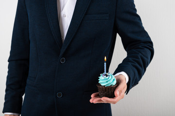 Businessman holding birthday cupcake with birning candle. Business greeting card. 1 year. Corporate party. Copy space