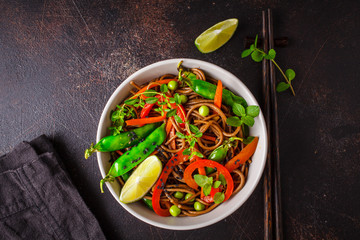 Vegan buckwheat soba noodles with vegetables on dark background, top view.