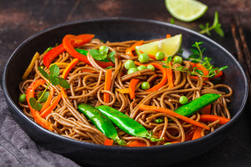 Vegan buckwheat soba noodles with vegetables in black plate on dark background.