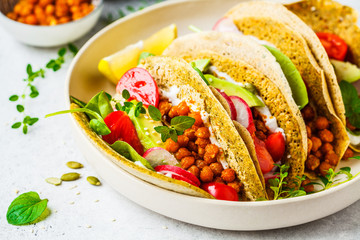 Vegan tacos with baked chickpeas, avocado, sauce and vegetables on white background.