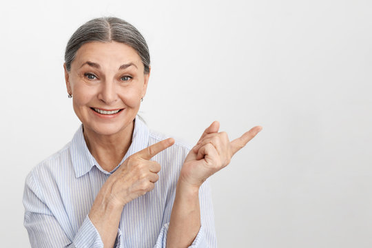 Isolated studio image of charismatic excited elderly female Human Resources expert with gray hair pointing index fingers to the right and smiling broadly, friendly showing you way to success