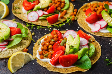 Vegan tacos with baked chickpeas, avocado, sauce and vegetables on dark background.