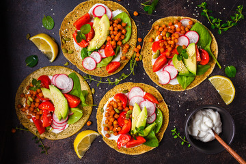 Vegan tacos with baked chickpeas, avocado, sauce and vegetables on dark background, top view.