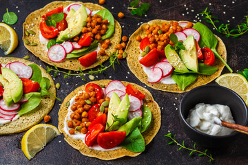 Vegan tacos with baked chickpeas, avocado, sauce and vegetables on dark background.
