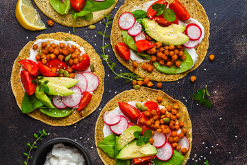 Vegan tacos with baked chickpeas, avocado, sauce and vegetables on dark background, top view.