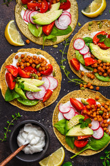 Vegan tacos with baked chickpeas, avocado, sauce and vegetables on dark background, top view.