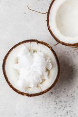 Coconut oil in a coconut shell on gray background, top view.