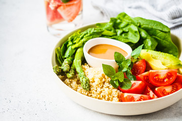 Green salad with quinoa, avocado and asparagus in a white bowl.