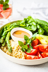 Green salad with quinoa, avocado and asparagus in a white bowl.