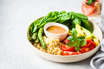 Green salad with quinoa, avocado and asparagus in a white bowl.