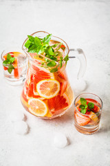 Grapefruit lemonade with lemon and mint in glass jug.