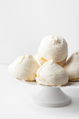 Home baked meringue cookies on cake stand on white table wall background. French Italian Swiss desserts cuisine confection. Airy elegant style. Recipe poster baking course template
