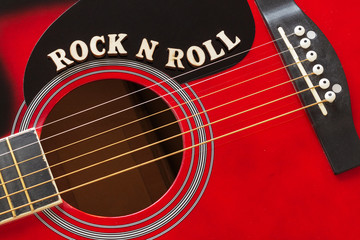 Words Rock N Roll with wooden letters, closeup on a surface of red acoustic guitar. Music entertainment background.
