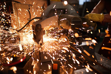 Close-up of metalworker using circular saw while cutting metal in workshop, sparkles flying all over place
