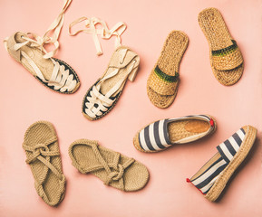 Variety of trendy woman's summer shoes. Flat-lay of espadrilles, sandals, flip flops made of natural materials over pastel pink background, top view. Summer season footwear apparel concept