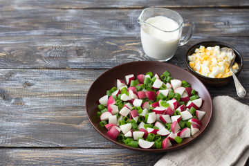 Fototapeta na wymiar Fresh radish salad with green onions on a wooden background, rustic style