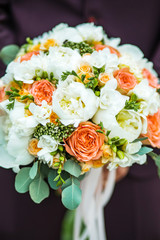 A beautiful bouquet of mixed flowers in the hand of the groom in a suit. Wedding bouquet of fresh flowers for the bride