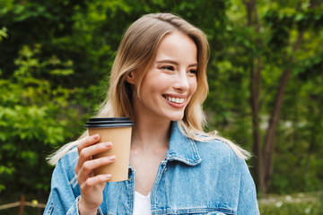 Photo closeup of cute caucasian woman drinking coffee while walking in green park