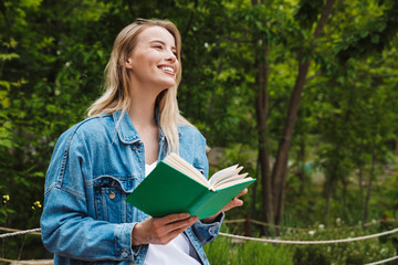 Photo of nice happy woman reading book while sitting on bench in green park