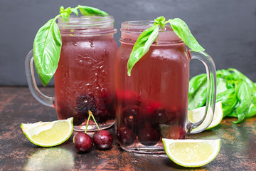 Homemade iced cherry lemonade with aromatic basil and line isolated on dark vintage background.  Summer refreshing drink.
