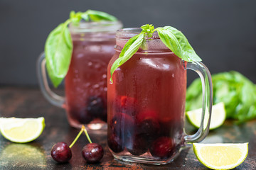 Iced homemade cherry lemonade with lime and basil isolated on dark vintage background.