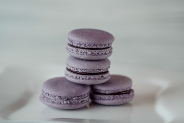 FRENCH CAKES MACARONS PURUPURAL AND BLUEBERRY ON A WHITE PLATE ON BLURRED WOODEN BACKGROUND