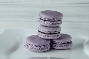 Fototapeta na wymiar FRENCH CAKES MACARONS PURUPURAL AND BLUEBERRY ON A WHITE PLATE ON BLURRED WOODEN BACKGROUND