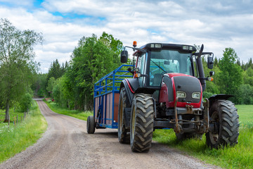 Tractor with trailer on the country side road with green trees and cloudy sky