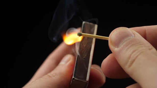 The match moves on the side of the matchbox and light the fire. Closeup. Shallow depth of field. Slow motion.