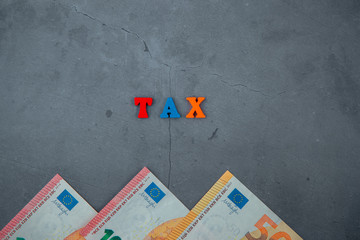 The multicolored tax word is made of wooden letters on a grey plastered wall background.
