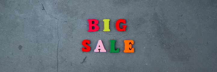 The multicolored big sale word is made of wooden letters on a grey plastered wall background.
