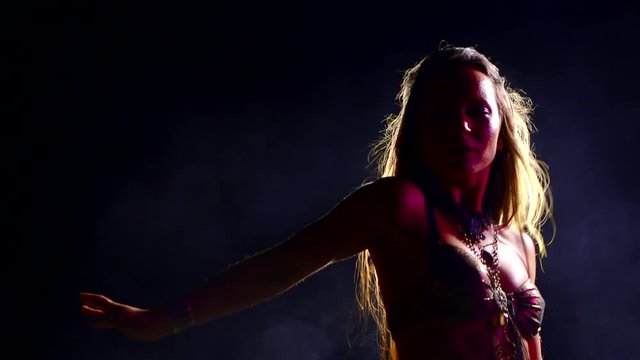 exotic belly dancer is moving in dark and smoke studio, wriggling her slim body