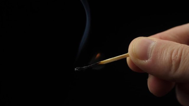 Smoke from Match lighting and burning till the end and finally disappears from the flame on black background. The match lights up, burns and goes out. Burning match stick lights and then blown out.