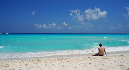 Fototapeta na wymiar Man sitting on the Caribbean sea sandy beach, Cancun, Mexico.