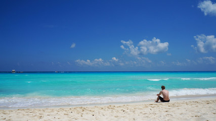Man sitting on the Caribbean sea coast, Cancun sand beach, Mexico.